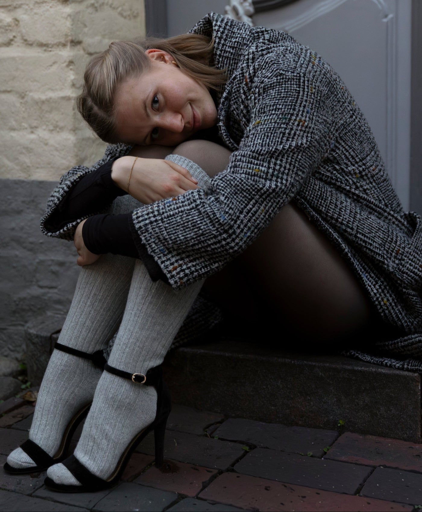 Woman sitting on a step wearing a checkered coat and high heels.